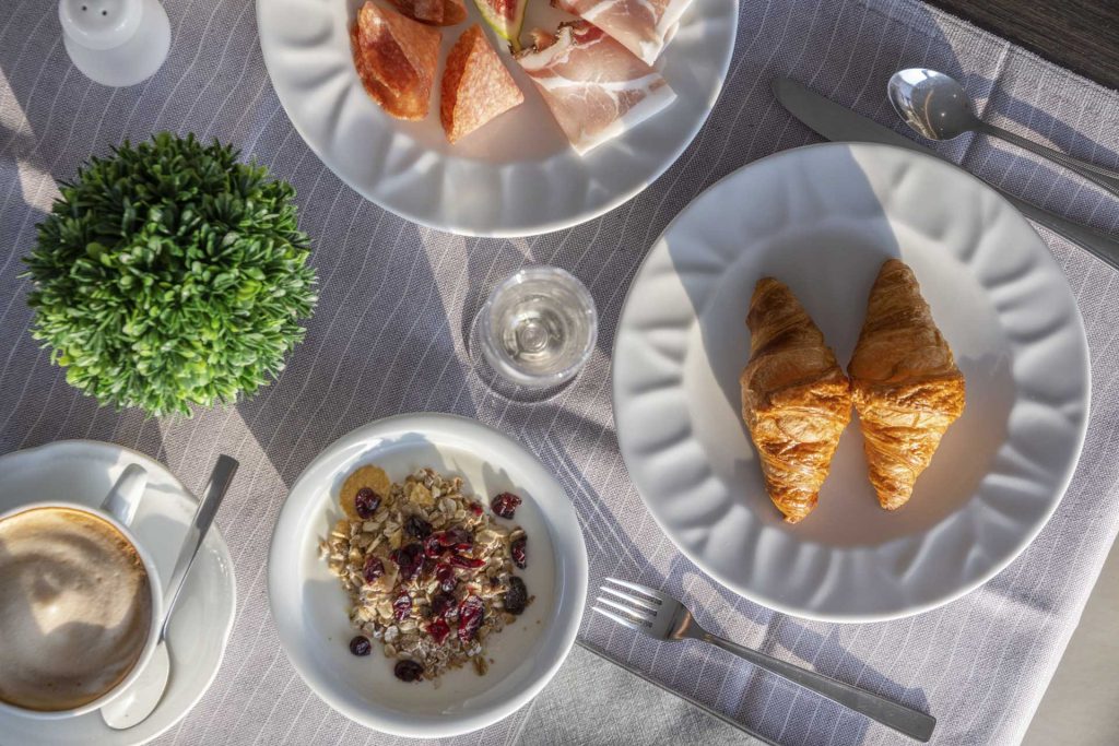 Ein gedeckter Tisch mit Croissants, Schinken, Müsli, Kaffee und einer kleinen Pflanze. Genussvoller Frühstücksaufbau.