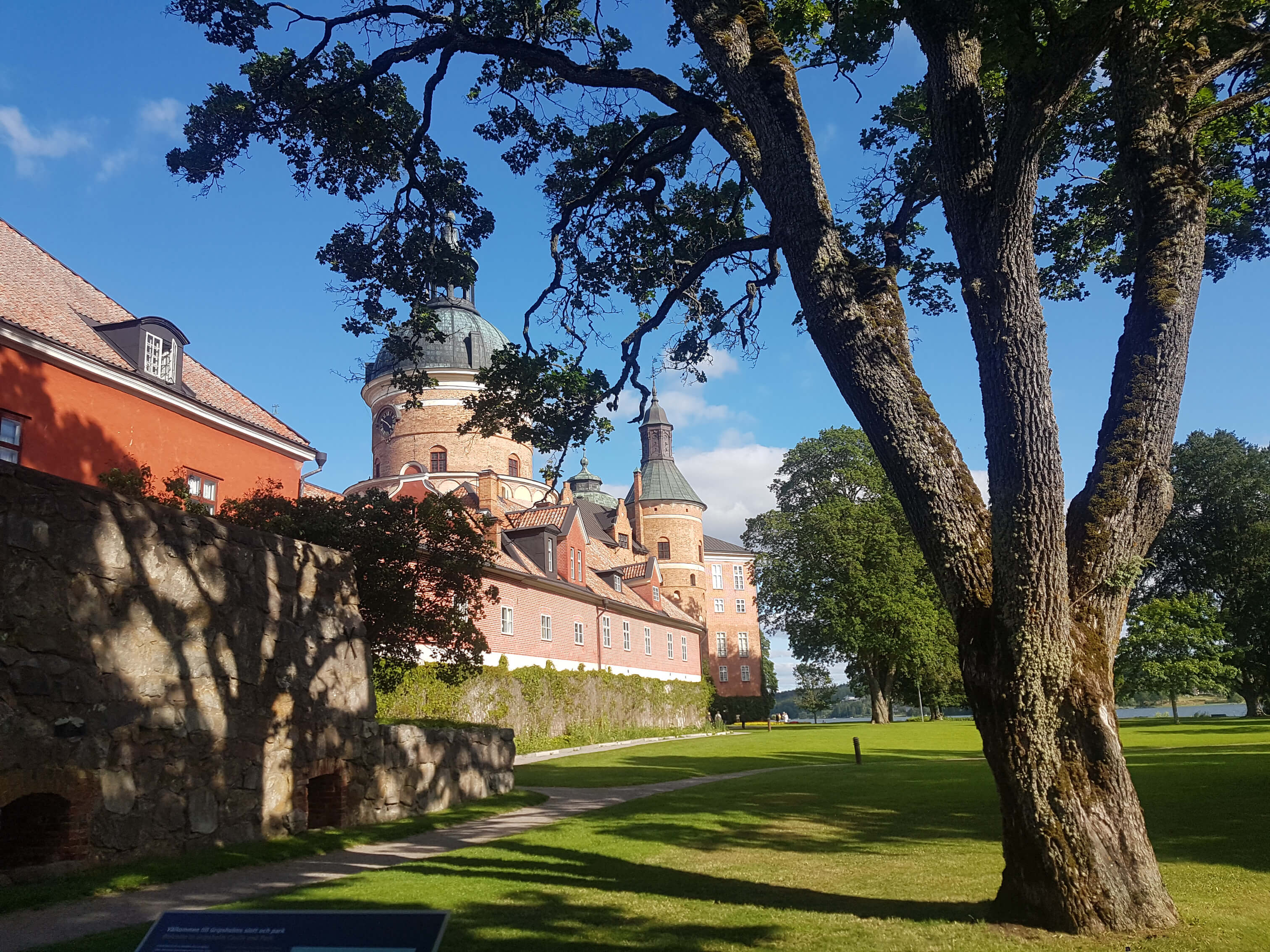 Ein historisches Schloss mit bunten Fassaden, umgeben von Bäumen und grünem Rasen unter blauem Himmel.