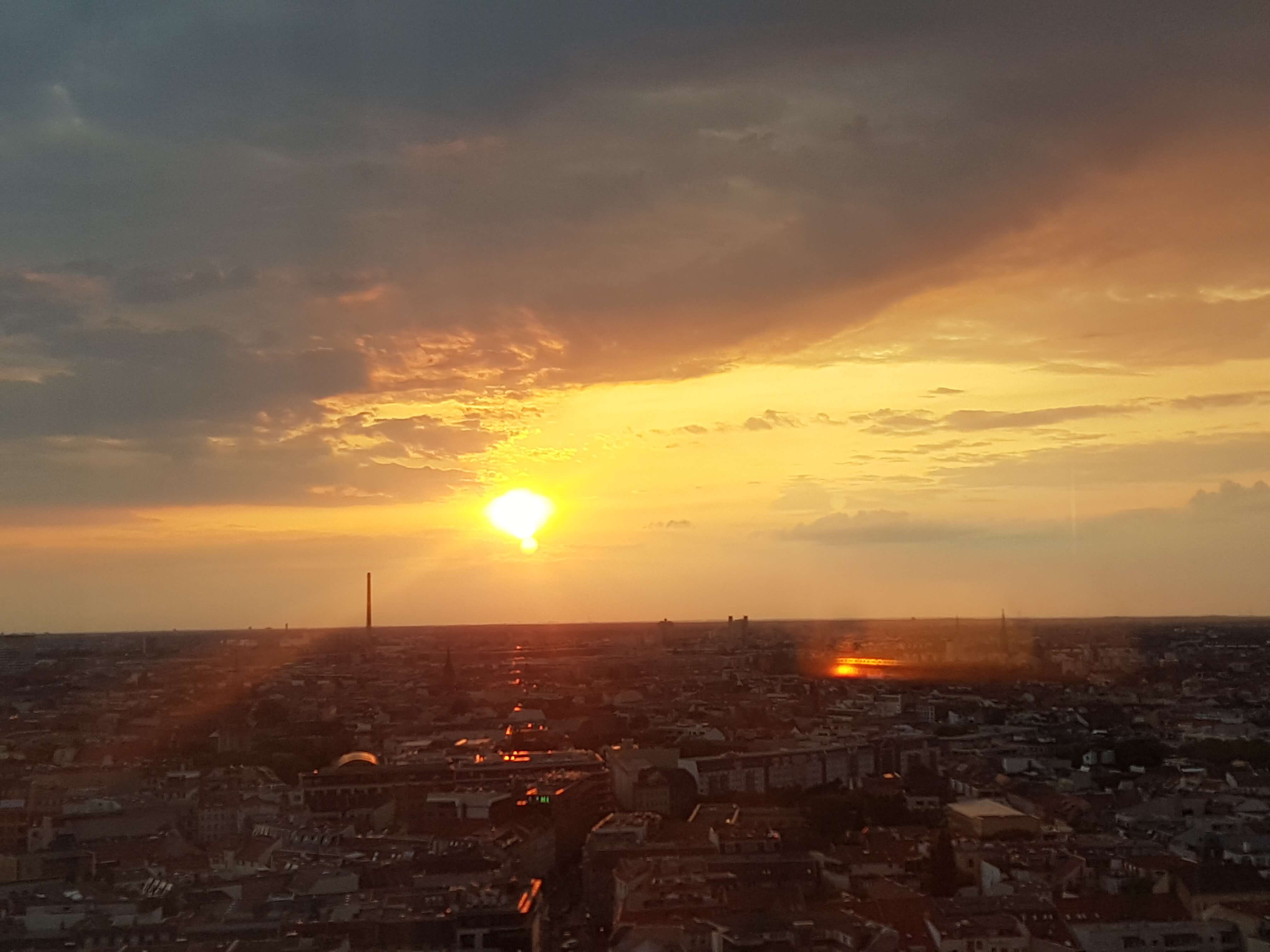 Ein malerischer Sonnenuntergang über einer Stadt, mit orangefarbenen Wolken und der Silhouette von Gebäuden.