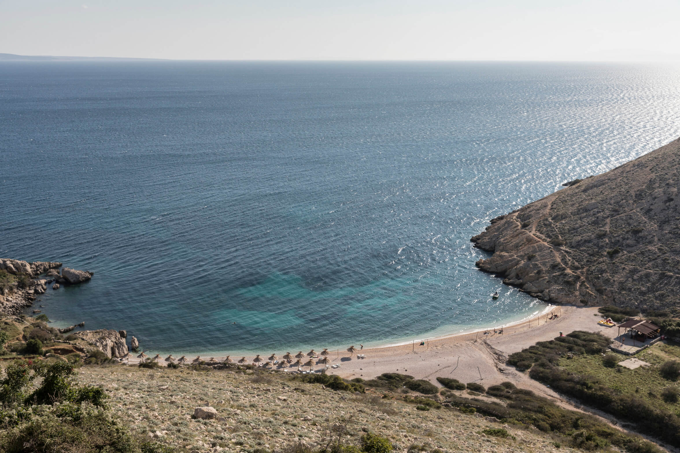 Eine ruhige Küstenlandschaft mit klarem Wasser, einem kleinen Strand und einer sanften Hügelkette im Hintergrund.