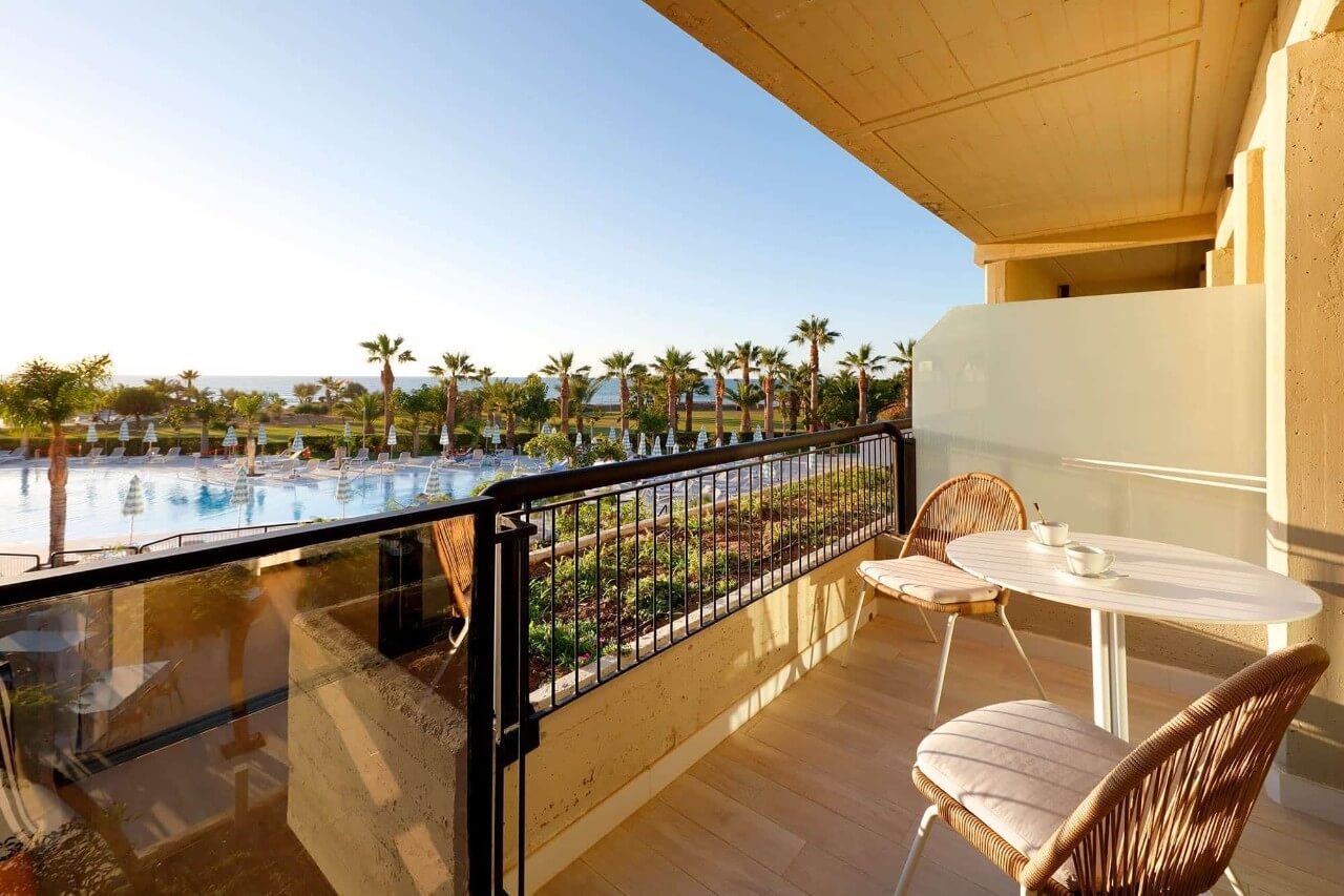 Balkon mit Blick auf den Pool und Palmen, einladender Tisch und Stühle für entspannte Momente.