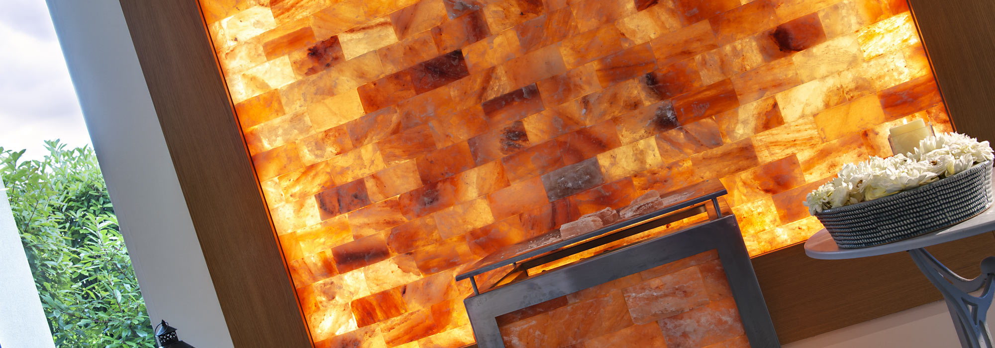 Wand aus orangem Salzstein, mit Blumen und Kerze auf einem Tisch, entspannende Atmosphäre und modernes Design.