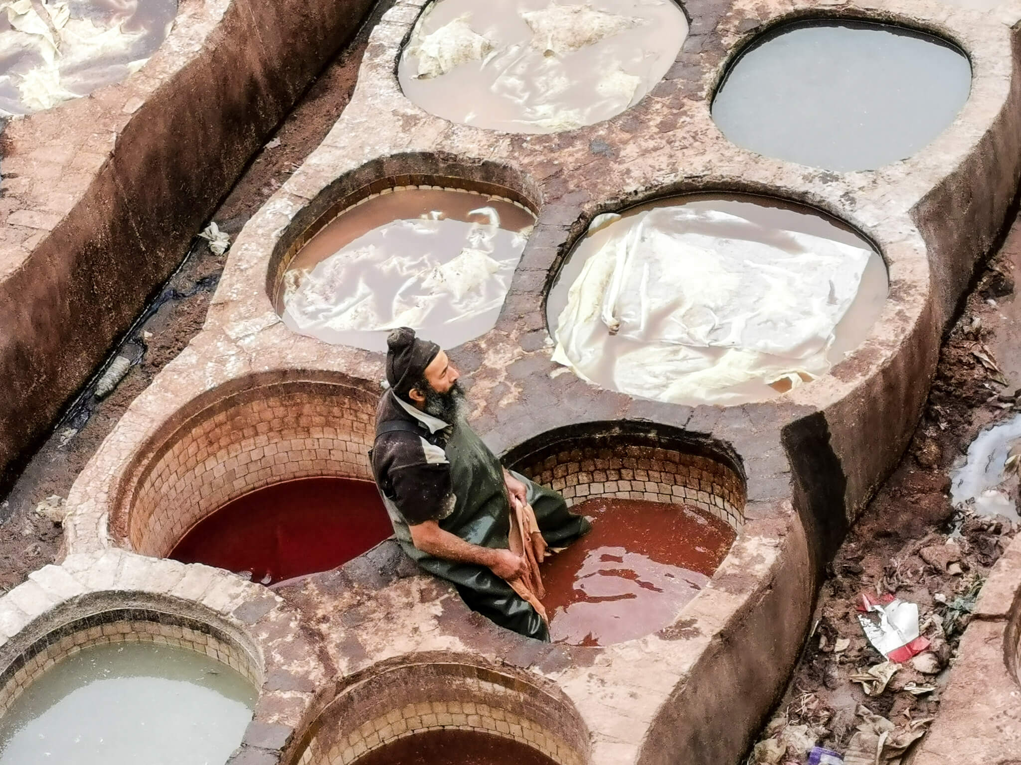 Ein Arbeiter sitzt in einem Farbtrog, umgeben von verschiedenen Färbegefäßen in einer traditionellen Gerberei.