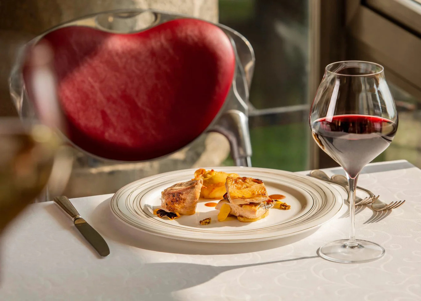 Ein eleganter Tisch mit einem Teller Angerichtetem und einem Glas Rotwein neben einem roten Stuhl.