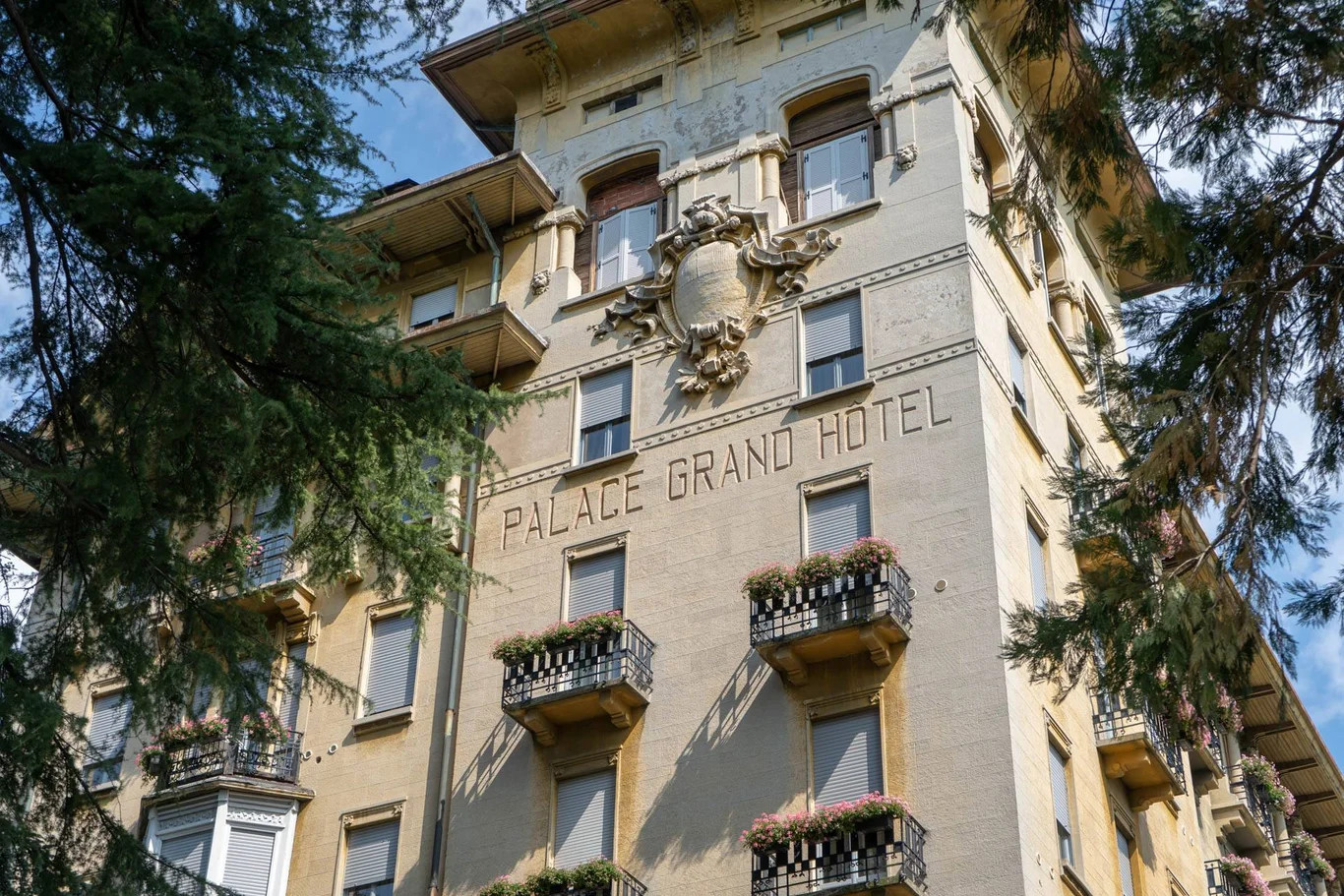 Ein altes Hotelgebäude mit der Aufschrift "Palace Grand Hotel" und blühenden Balkonen.
