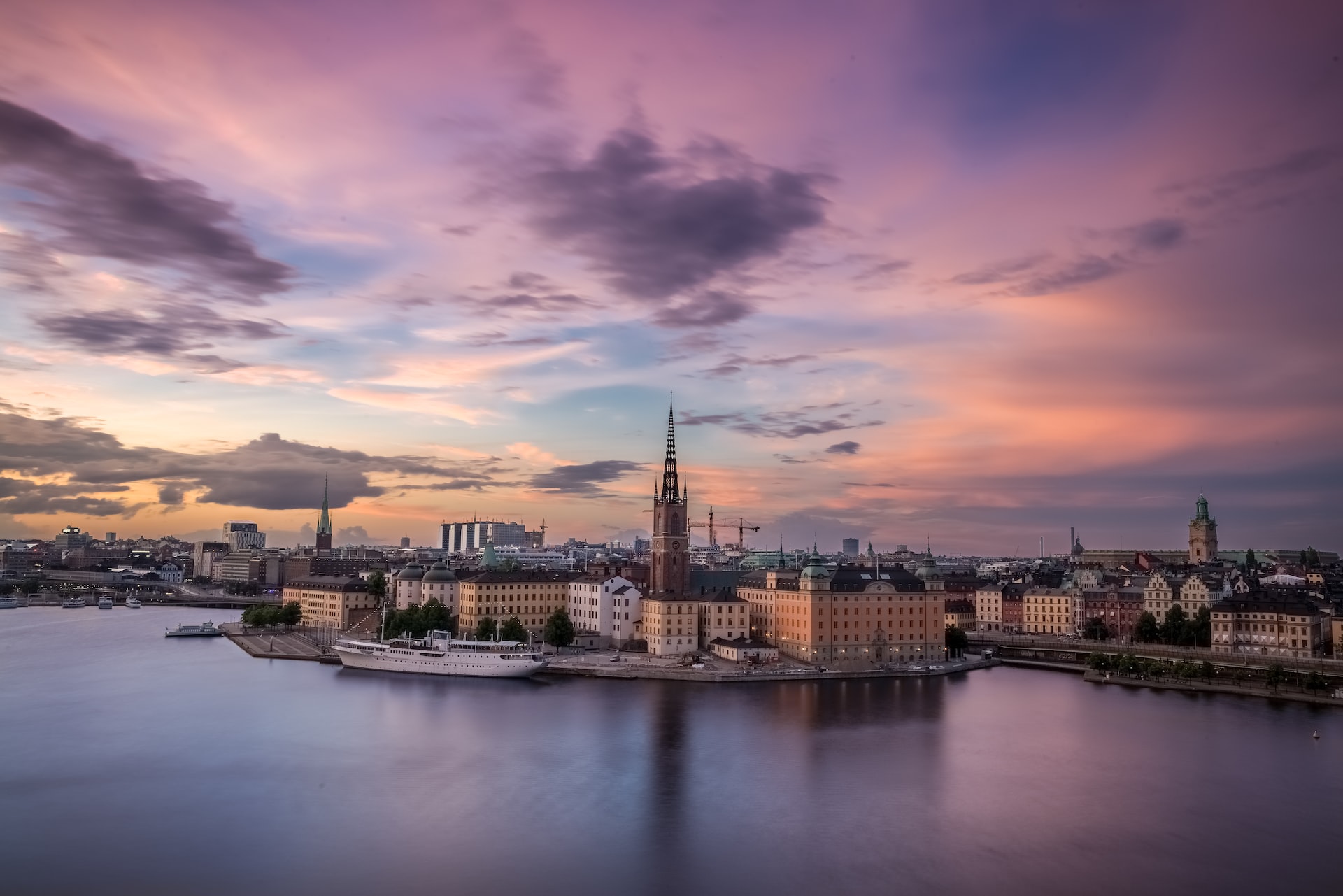 Stockholm bei Sonnenuntergang, mit farbenfrohem Himmel, Wasser und historischen Gebäuden am Ufer.