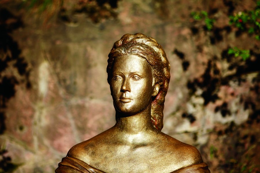 Eine bronzene Statue einer Frau mit einem fokussierten Ausdruck, vor einer natürlichen Felswand platziert.