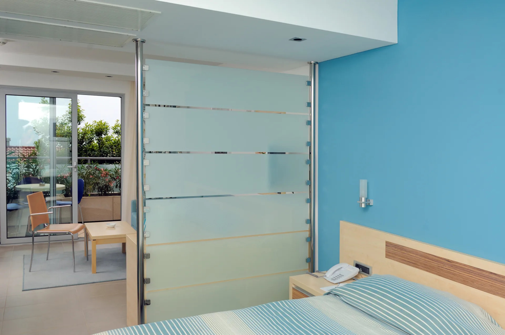 Modernes Schlafzimmer mit einer Glaswand, hellblauem Farbschema und Zugang zu einem Balkon. Komfortabel und stilvoll.