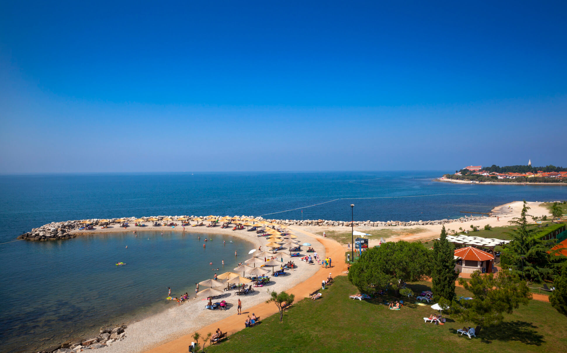 Ein sonniger Strand mit Liegen, Sonnenschirmen und einem klaren blauen Wasser, ideal für einen entspannten Tag.