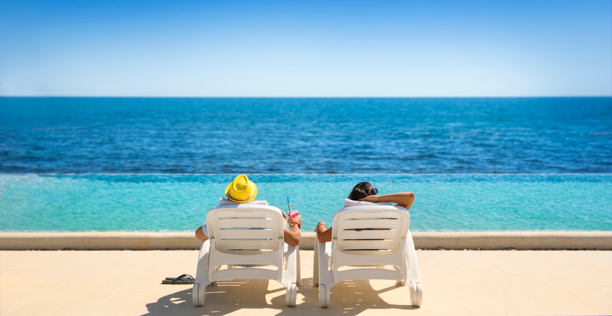 Zwei Personen entspannen auf Liegen mit Blick auf das Meer, ein sonniger Tag mit erfrischenden Getränken.