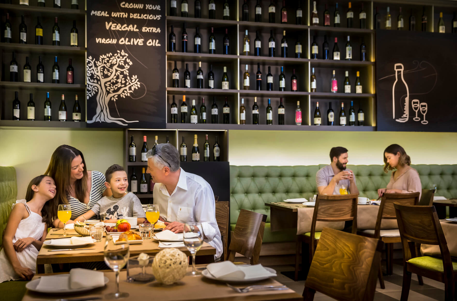 Eine Familie genießt eine Mahlzeit in einem modernen Restaurant mit Weinen im Hintergrund. Stimmungsvoll und einladend.