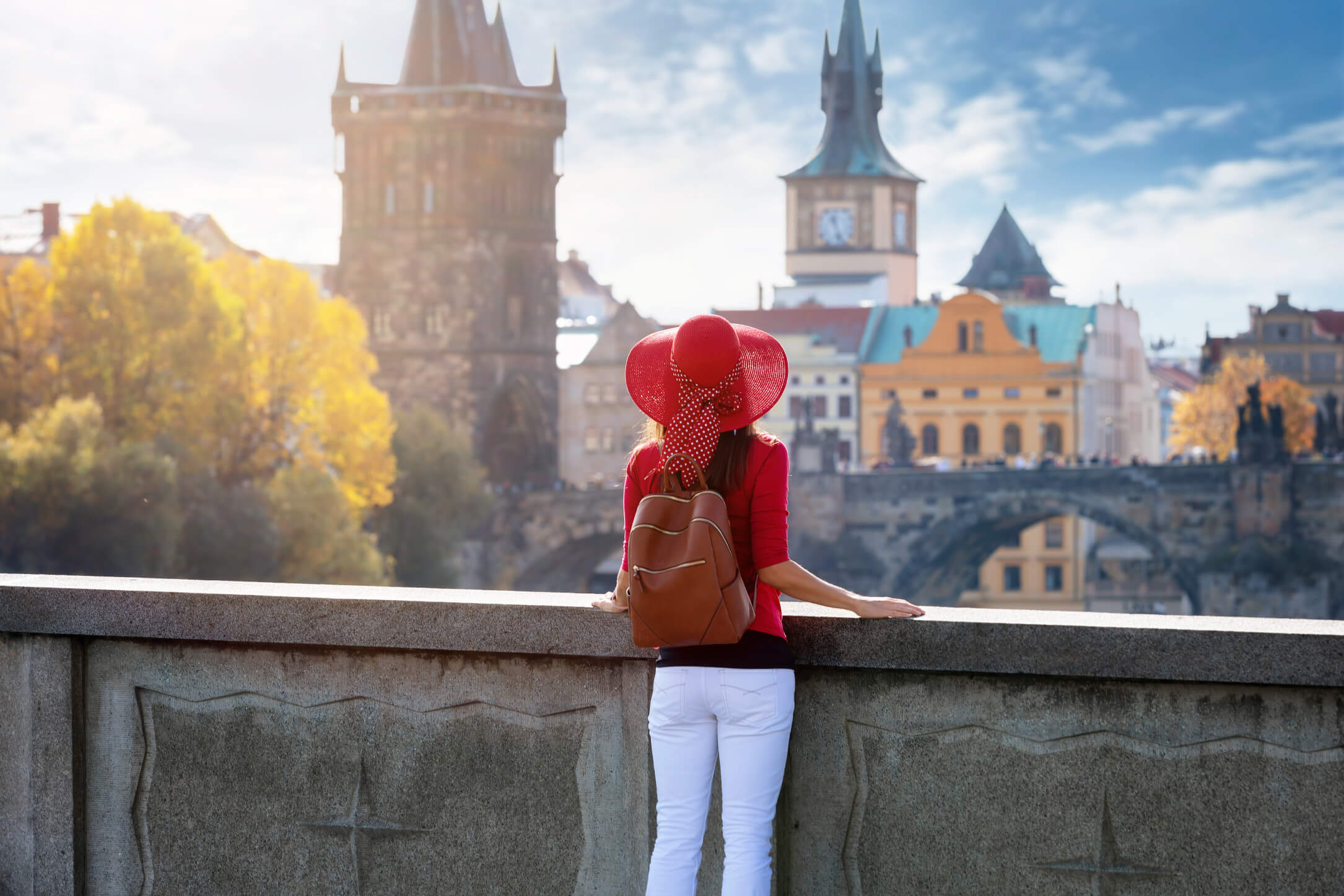 Eine Frau mit rotem Hut und Rucksack genießt die Aussicht auf die Stadt mit der Karlsbrücke im Hintergrund.
