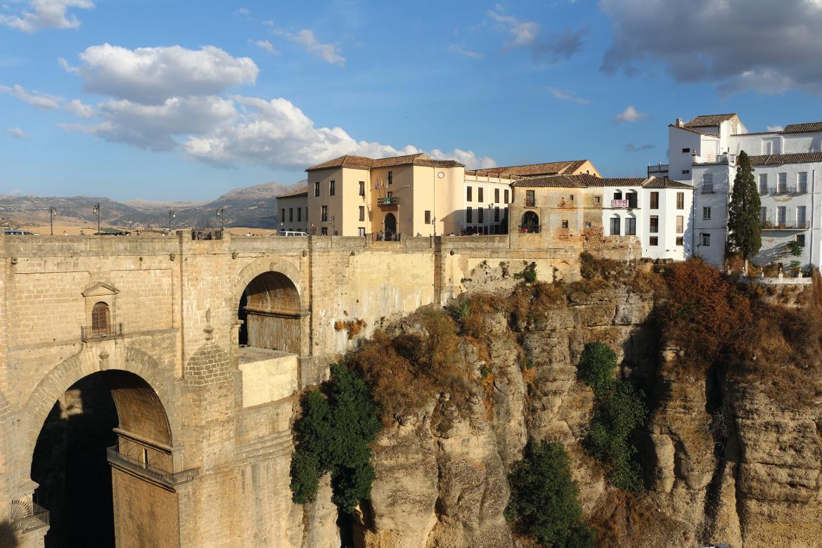 Eine beeindruckende Brücke verbindet historische Gebäude über einer tiefen Schlucht unter blauem Himmel.