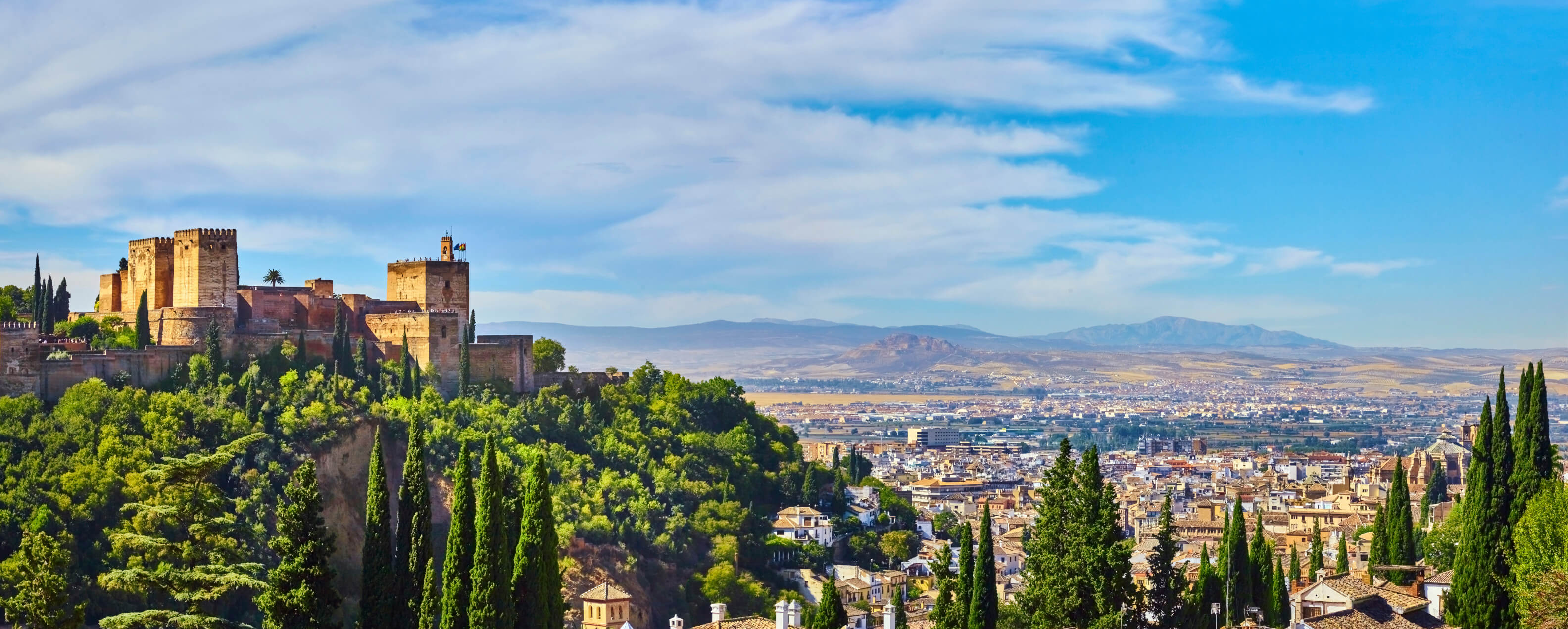Eine beeindruckende Landschaft mit der Alhambra und grünen Hügeln unter einem klaren, blauen Himmel.
