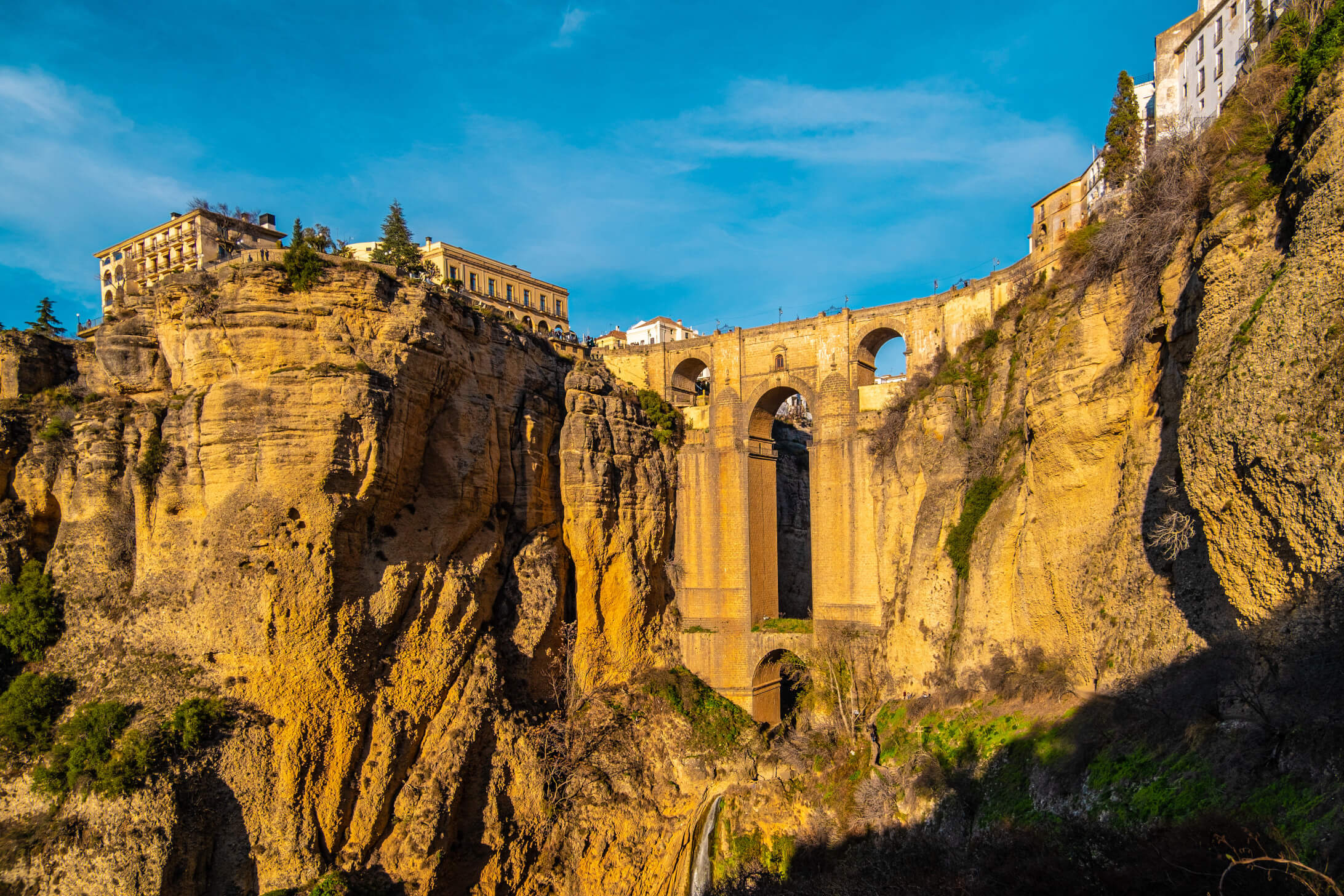 Eine beeindruckende Brücke über eine Schlucht, umgeben von malerischen Häusern und klarem, blauem Himmel.