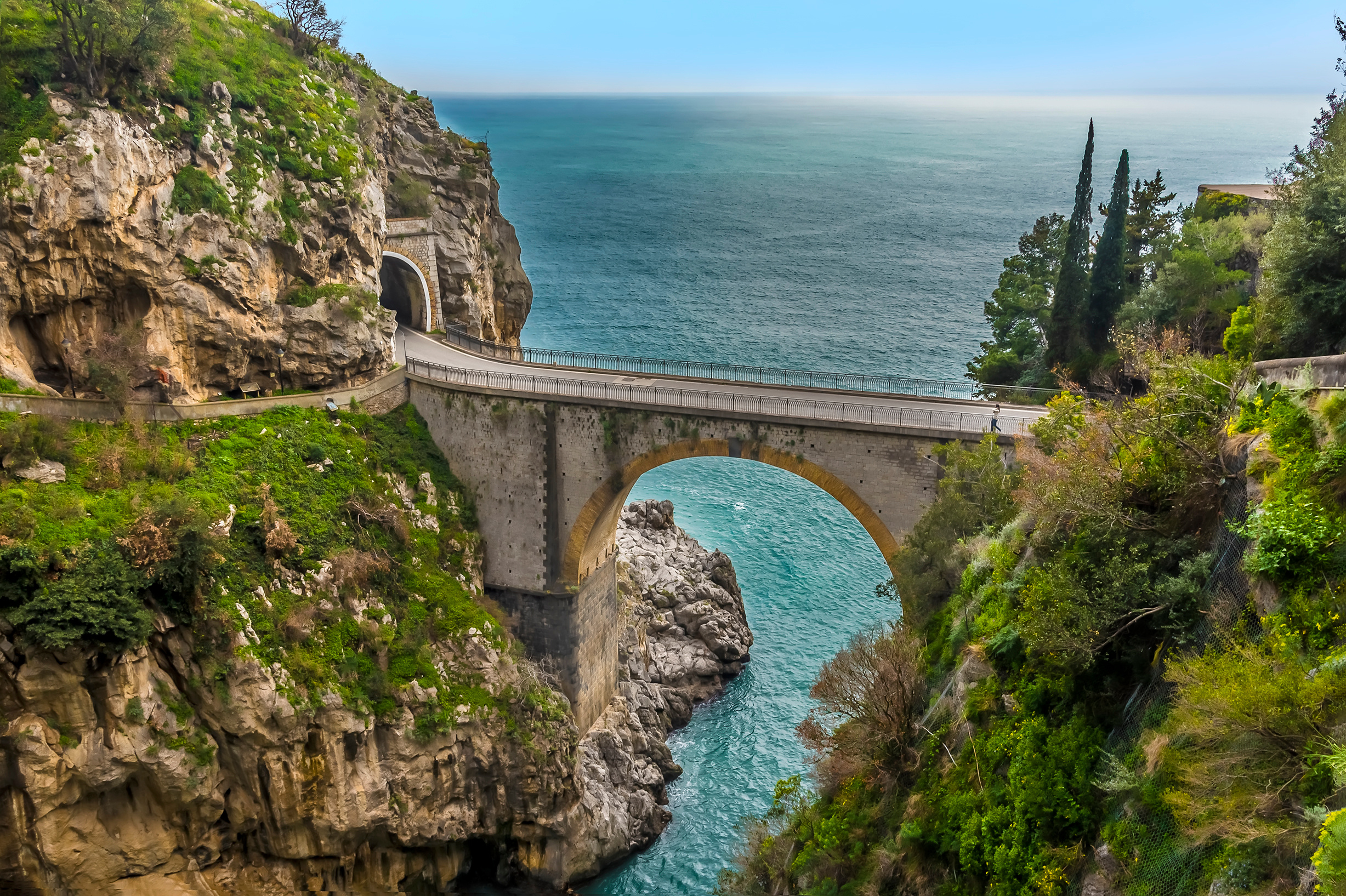 Eine beeindruckende Brücke verbindet zwei Felsen über dem glitzernden blauen Wasser des Meeres.