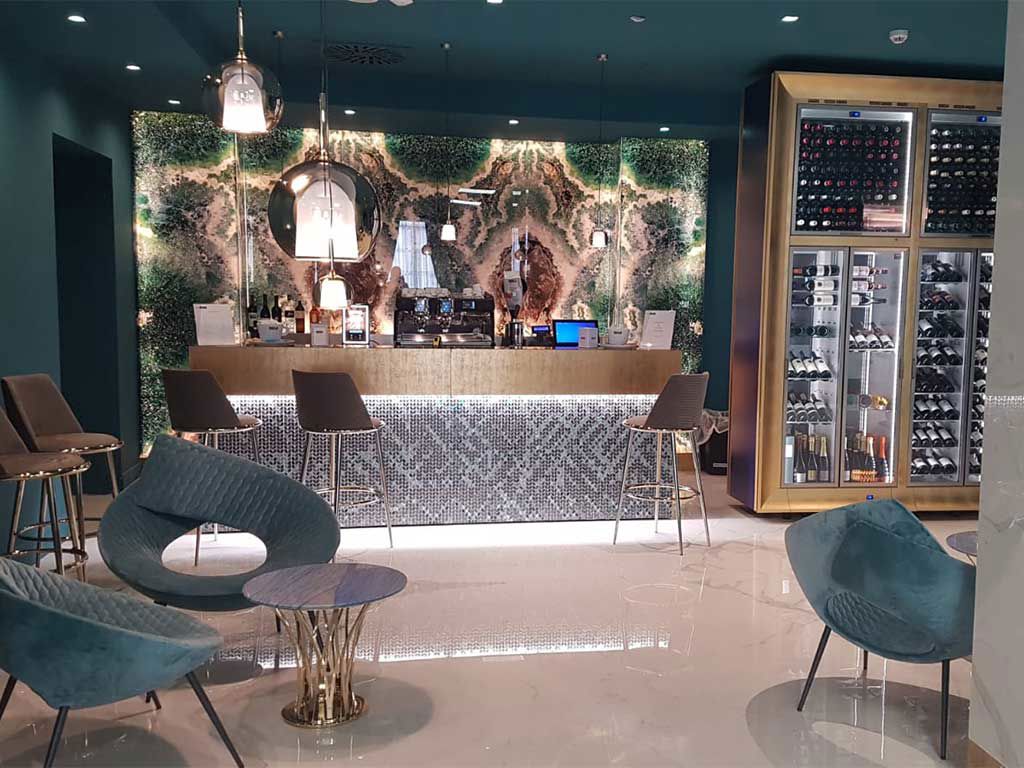 Elegante Bar mit grünem Wanddesign, stilvollen Möbeln und einer großen Weinregalvitrine. Moderner, einladender Stil.