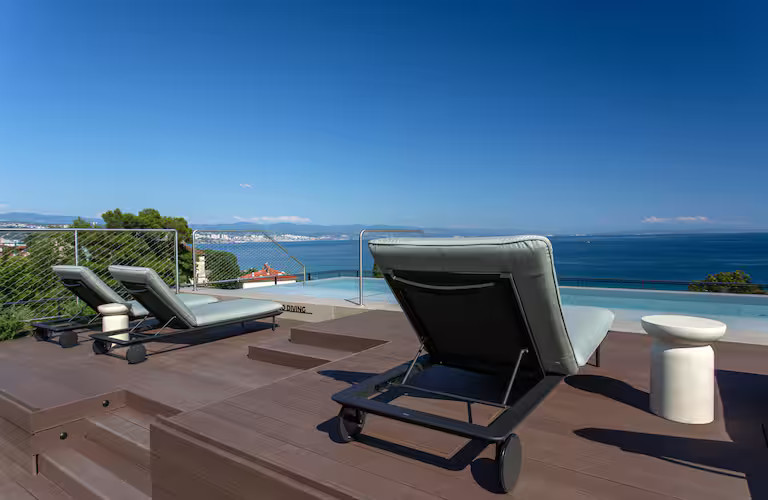 Moderne Liegen auf einer Terrasse mit Meerblick und klarem blauen Himmel, ideal zum Entspannen.