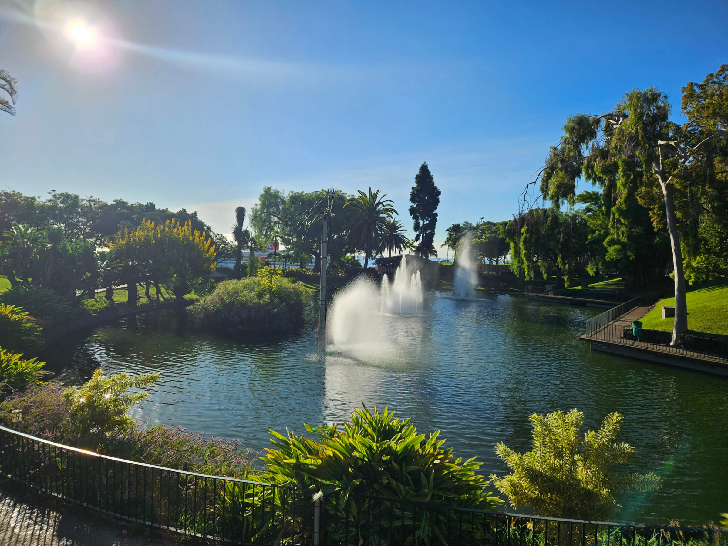 Ein schöner Park mit einem Teich, Springbrunnen, grünen Bäumen und klarem blauen Himmel. Sonnenlicht strahlt.