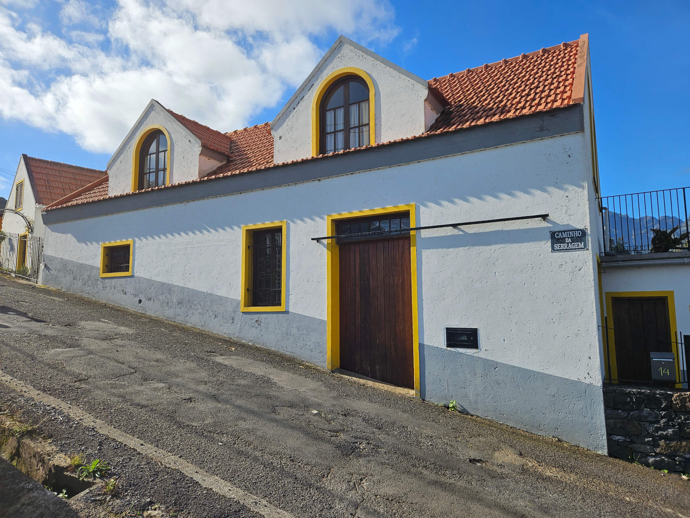 Ein historisches, zweigeschossiges Gebäude mit gelben Fensterrahmen und einem roten Dach auf einer schmalen Straße.