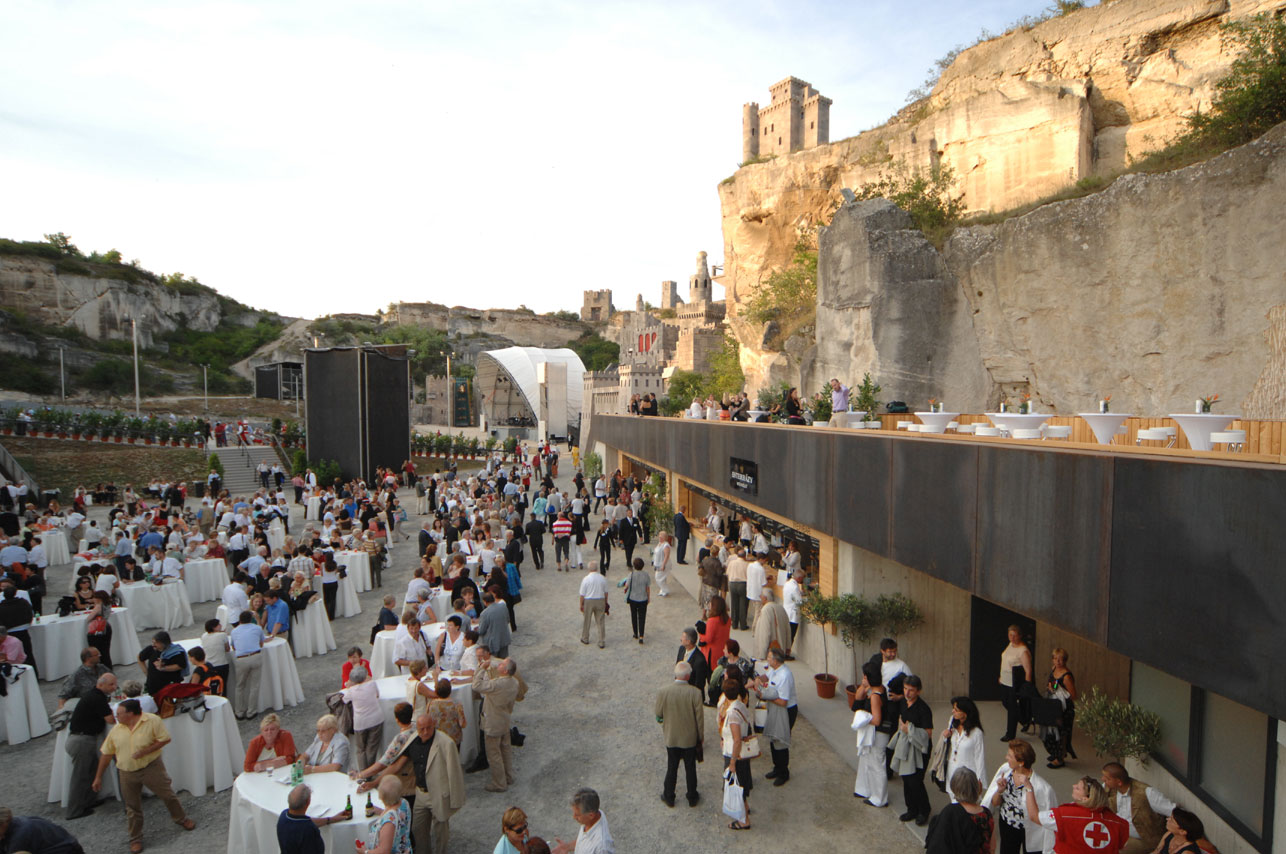 Eine große Menschenmenge feiert in einer malerischen Kulisse mit Tischen und einem Bühnenbereich.