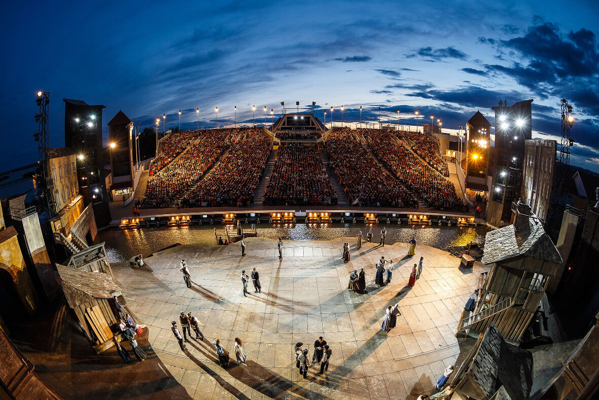 Eine beeindruckende Freiluftbühne vor einer großen Menschenmenge bei Dämmerung.