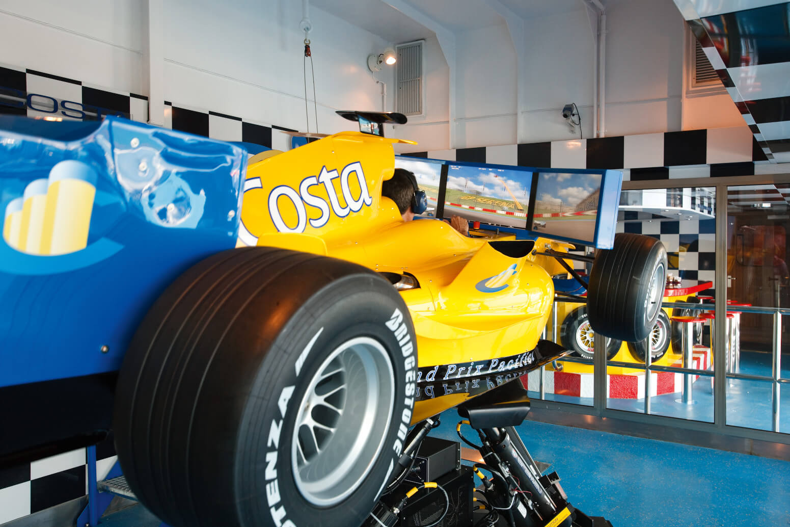 Ein Rennwagensimulator in einem modernen Raum mit Bildschirmen und einem gelben Rennwagen.