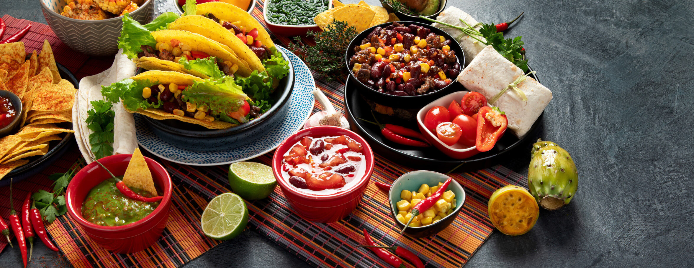 Bunte Auswahl an mexikanischen Speisen: Tacos, Guacamole, Salsa und frisches Gemüse auf einem rustikalen Tisch.