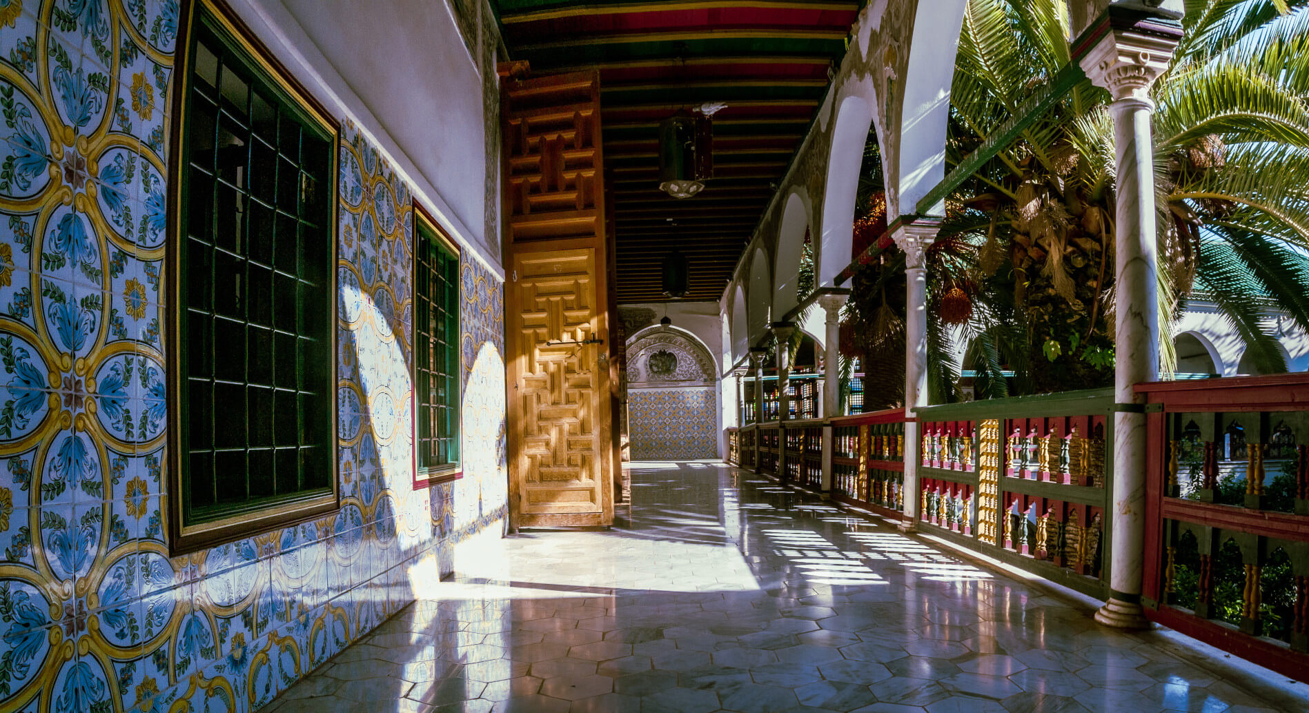Ein eleganter Flur mit bunten Fliesen, grünen Fenstern und einem Palmenhintergrund, der Lichtspiele wirft.
