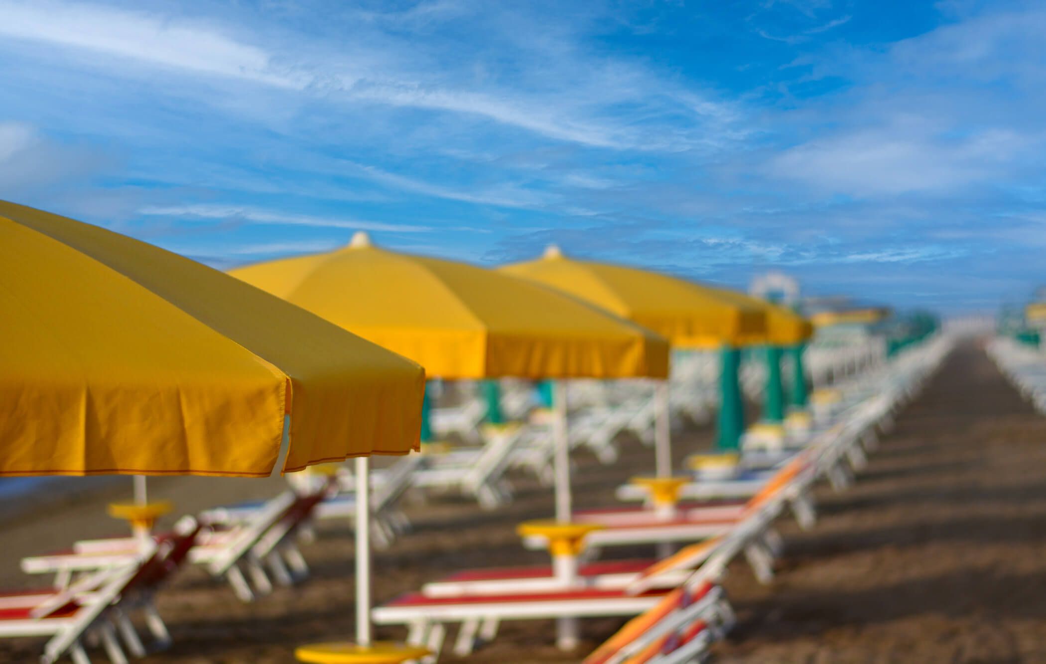 Bunte Sonnenschirme am Strand mit Liegen im Hintergrund unter einem klaren blauen Himmel.