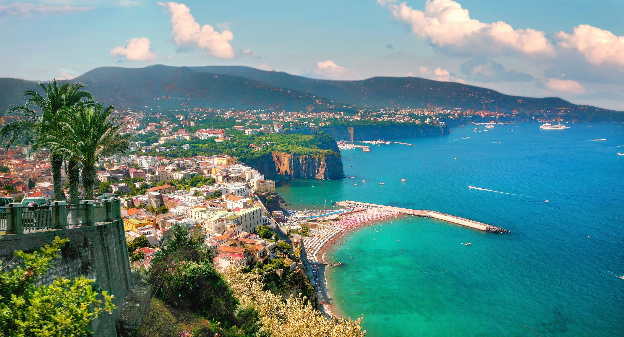 Eine malerische Küstenlandschaft mit bunten Häusern, Palmen und klarem, blauem Wasser.