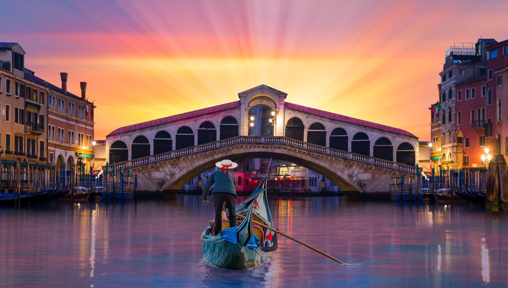Eine Gondel fährt unter der Rialtobrücke in Venedig bei einem wunderschönen Sonnenuntergang.