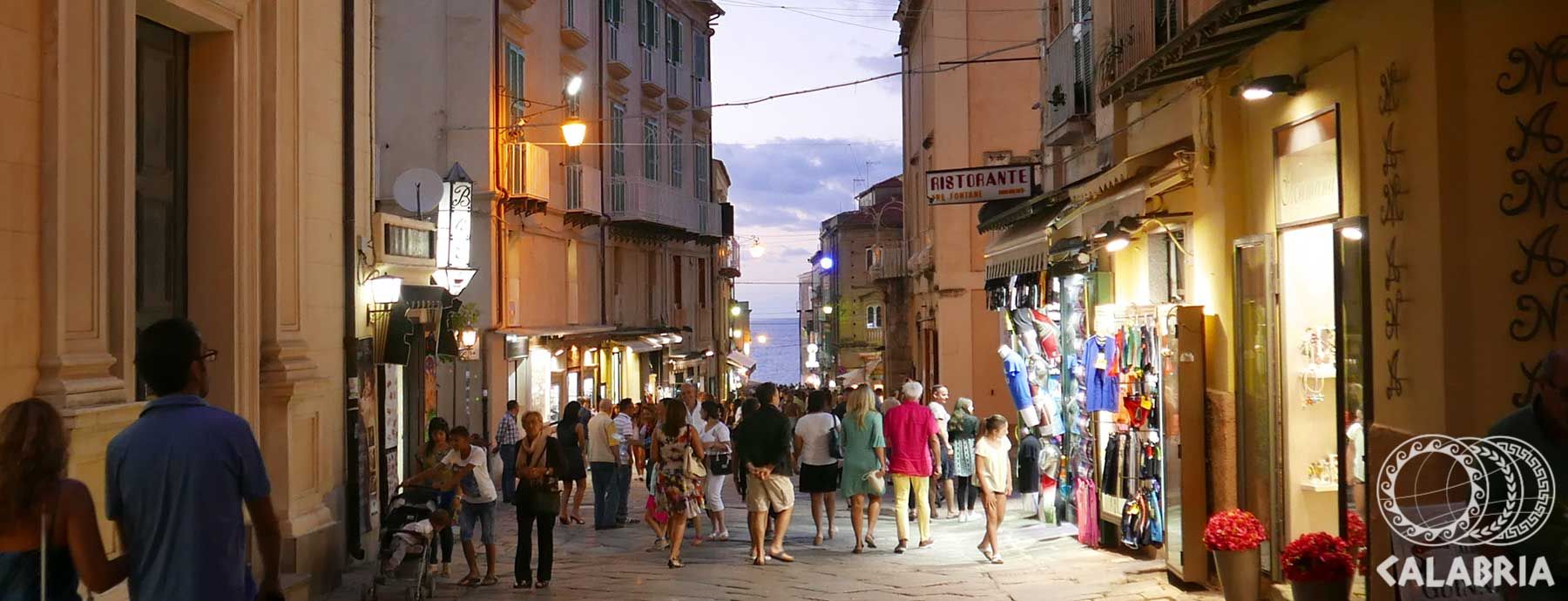 Eine belebte Straße mit Geschäften und Menschen bei Dämmerlicht, die eine lebhafte Atmosphäre vermittelt.