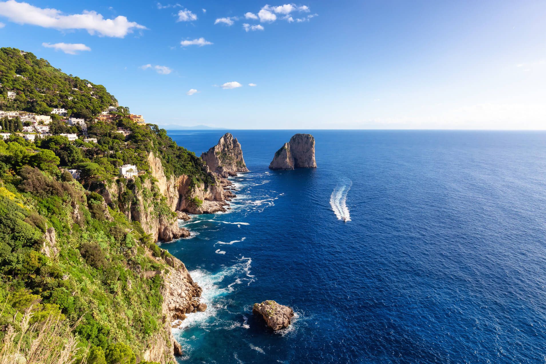 Wunderschöne Küstenlandschaft mit grünen Hügeln, blauen Wasser und markanten Felsen in der Ferne. Sonniger Himmel.