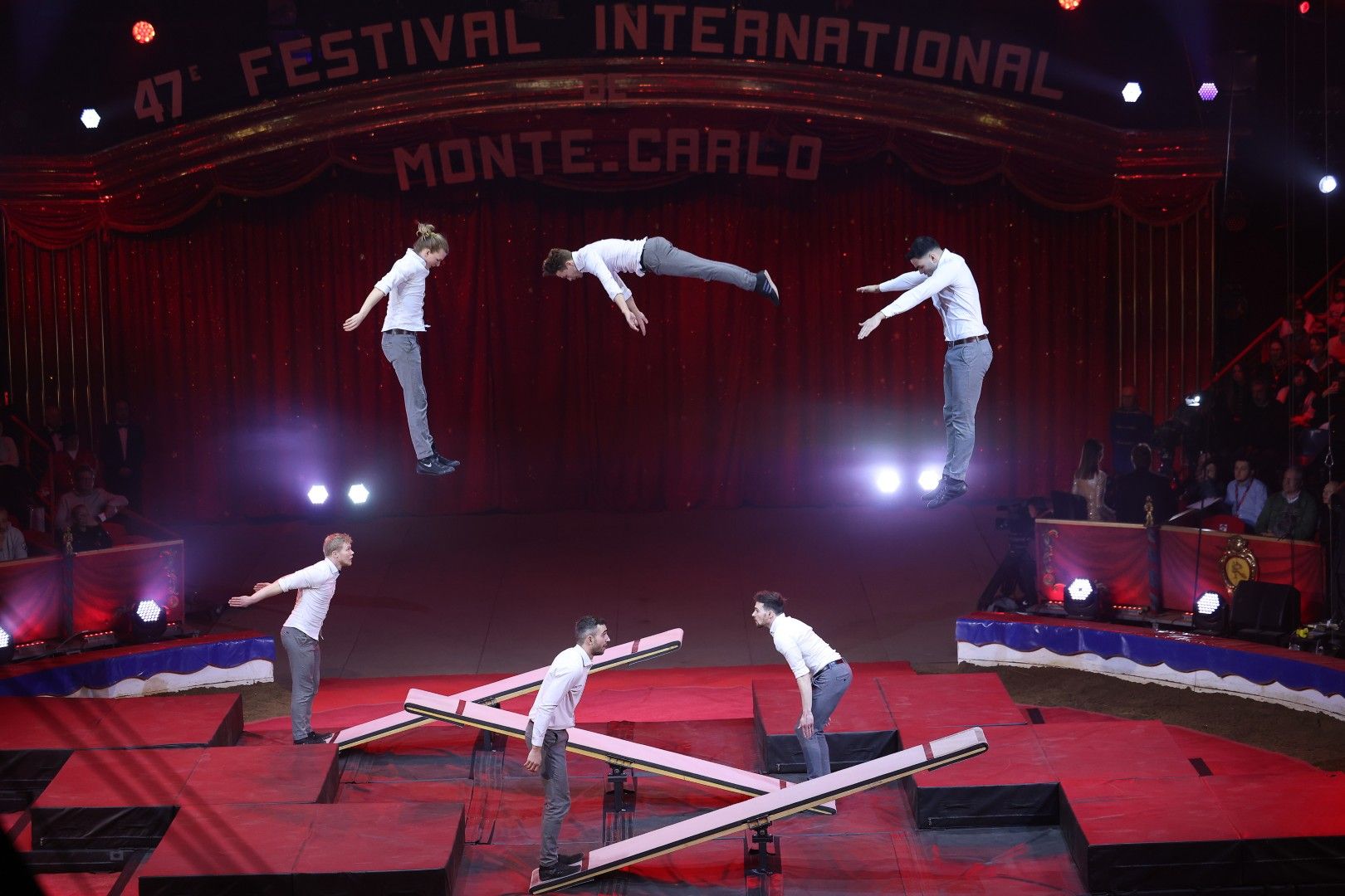 Sechs Akrobaten schweben in einem Zirkus, während sie auf einem Trampolin spektakuläre Sprünge ausführen.