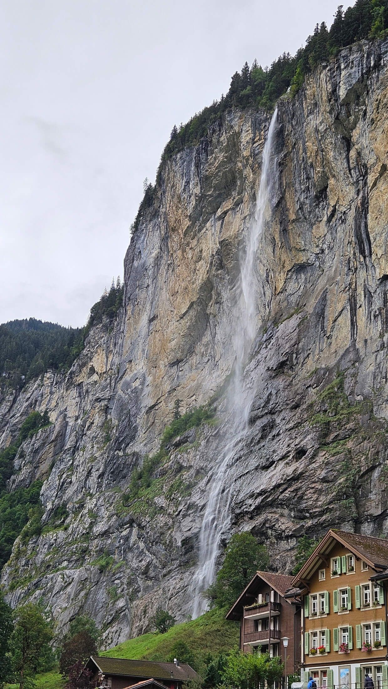 Ein Wasserfall fließt majestätisch von einer steilen Felswand in eine grüne Landschaft mit Häusern.