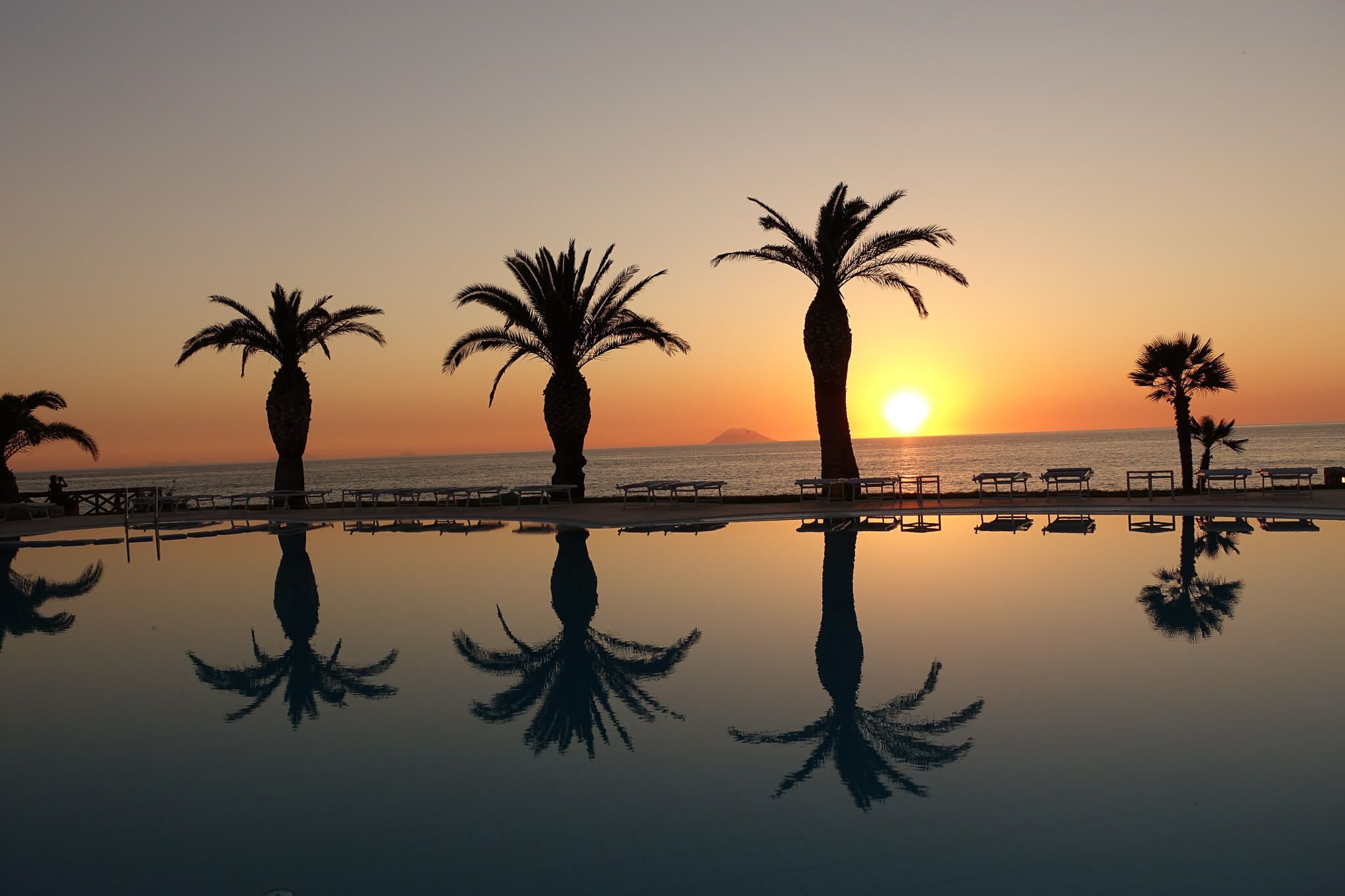 Sonnenuntergang über dem Meer mit Palmenreflektionen im Pool. Ruhige Atmosphäre und wunderschöne Farben.