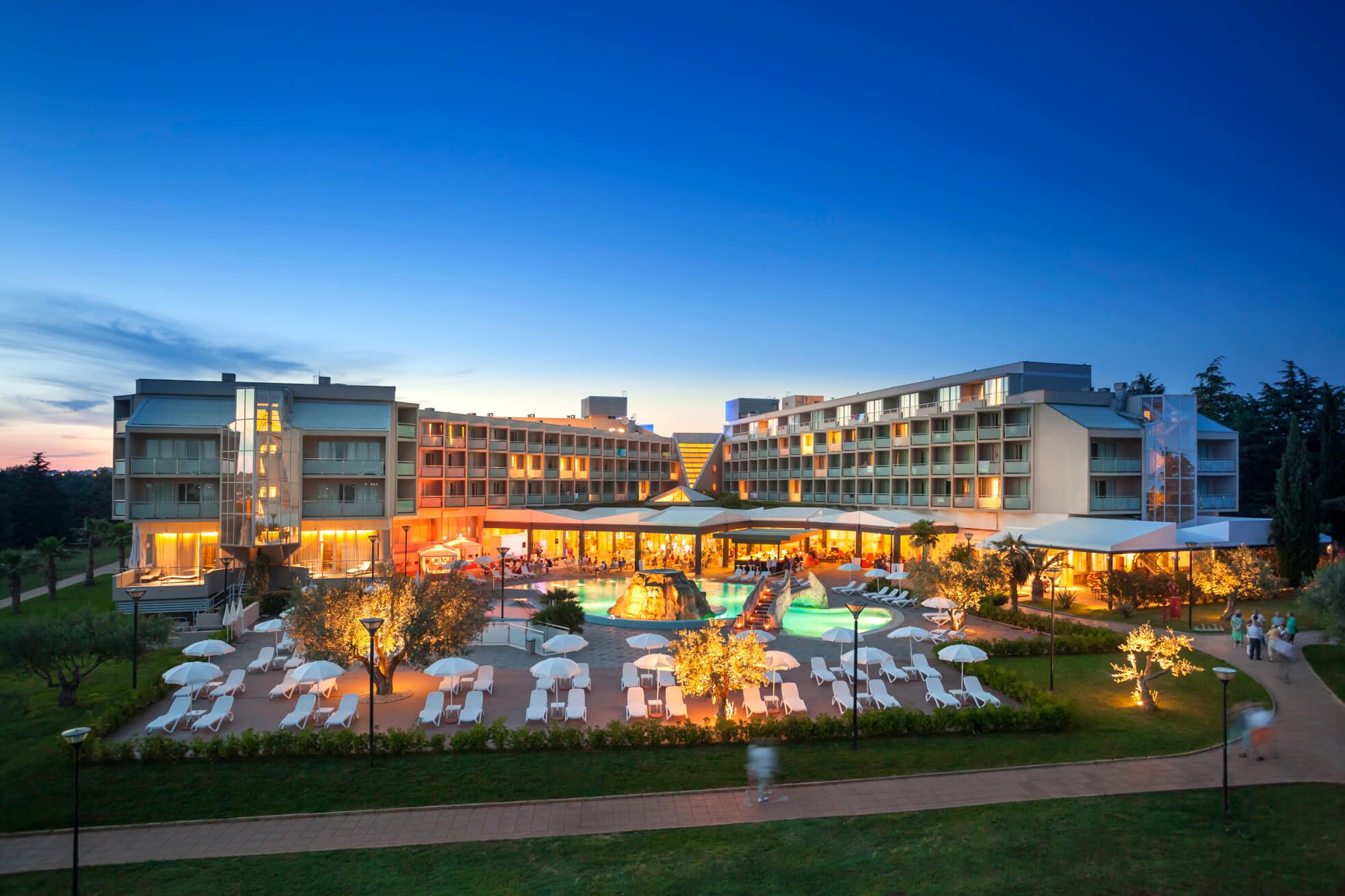 Ein modernes Hotel mit pool und Liegen, beleuchtet unter einem klaren Abendhimmel. Entspannende Atmosphäre im Freien.