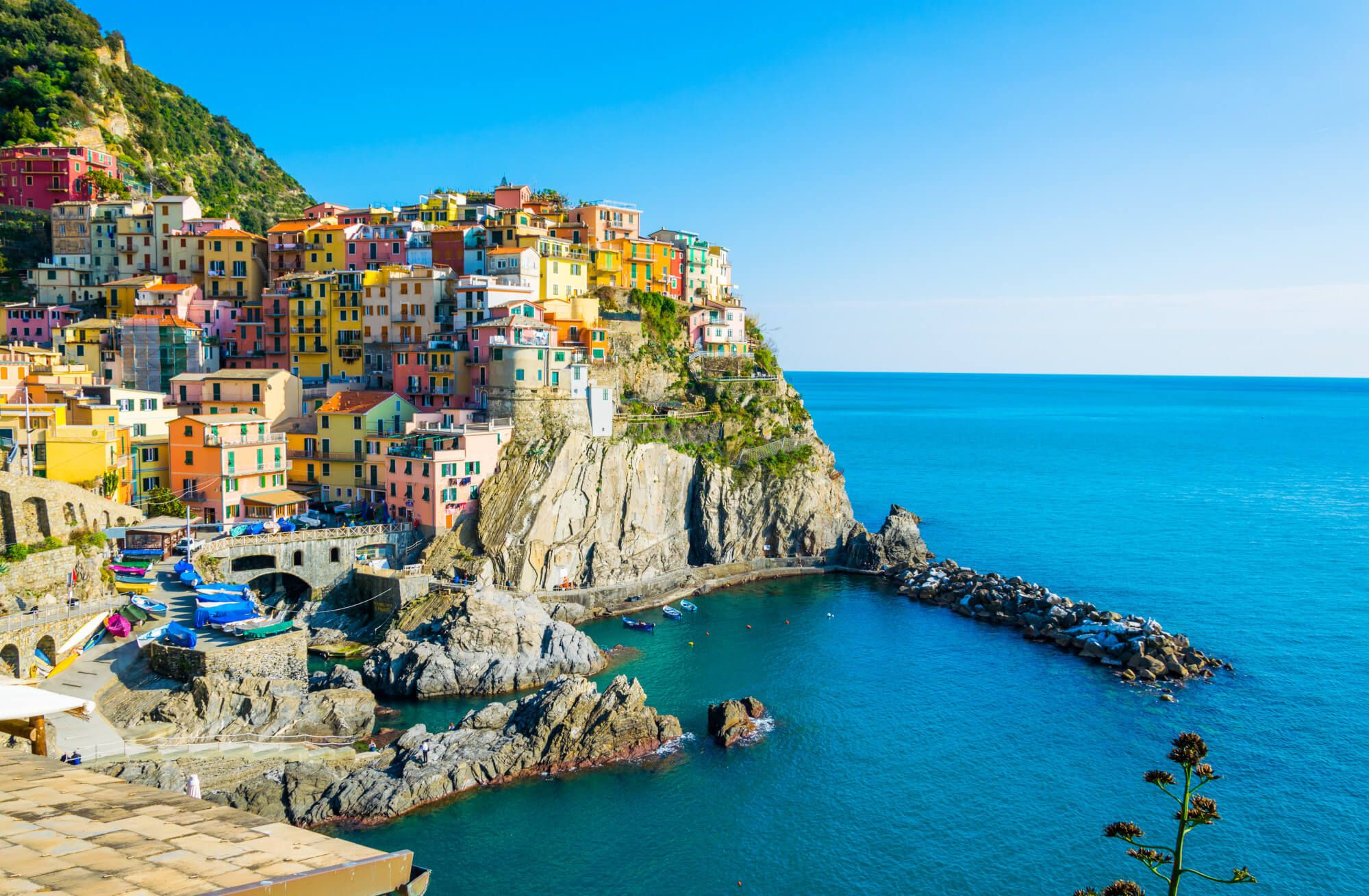 Bunte Häuser am Hang über einem klaren blauen Meer in Cinque Terre, Italien, unter strahlend blauem Himmel.