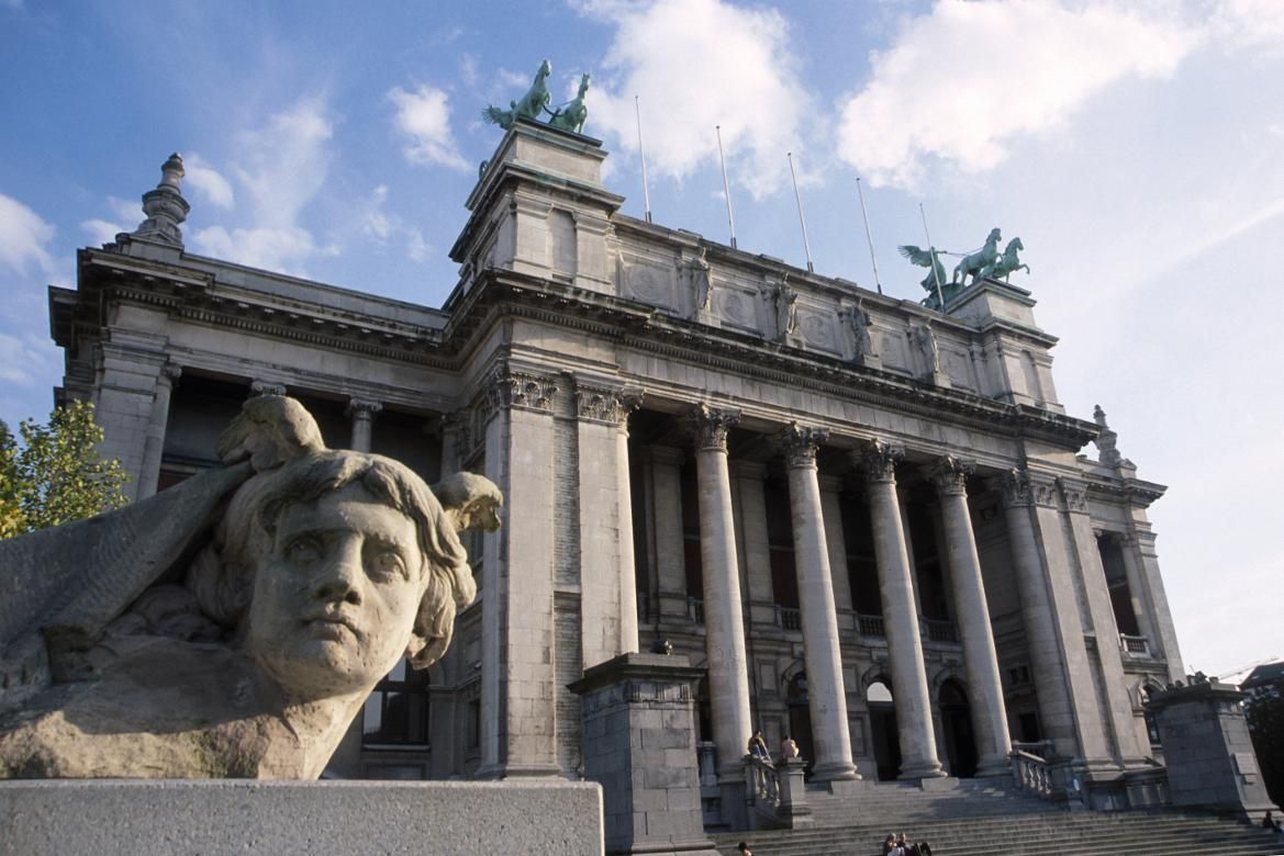 Ein monumentales Gebäude mit Säulen, Skulpturen im Vordergrund und einer klaren blauen Himmelsschicht.