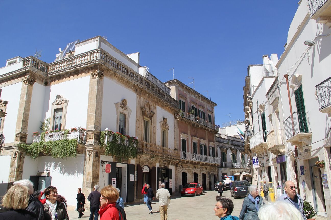 Ein malerischer Platz mit historischen Gebäuden, blühenden Balkonpflanzen und vielen Spaziergängern. Sonnenschein überall!