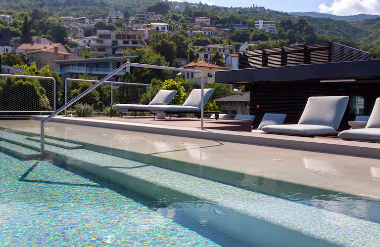 Elegantes Pool-Design mit Liegen, umgeben von grünen Hügeln und Wohnhäusern. Entspannung pur in schöner Natur.