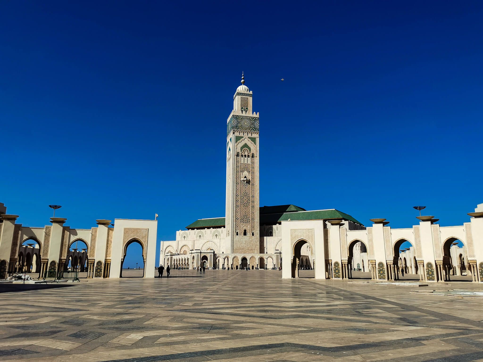Eine große Moschee mit einem hohen Minarett vor blauem Himmel und einem weiten Platz.