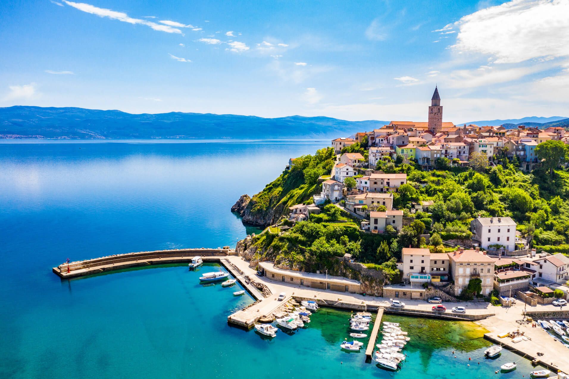 Eine malerische Küstenstadt mit bunten Häusern und einem ruhigen Hafen, umgeben von klarem Wasser und Bergen.