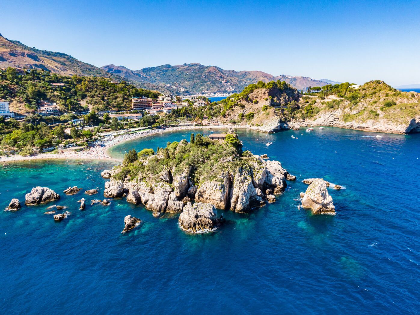 Eine malerische Küstenlandschaft mit klarem Wasser, Felsen und bewaldeten Hügeln im Hintergrund. Perfekter Urlaubsort!