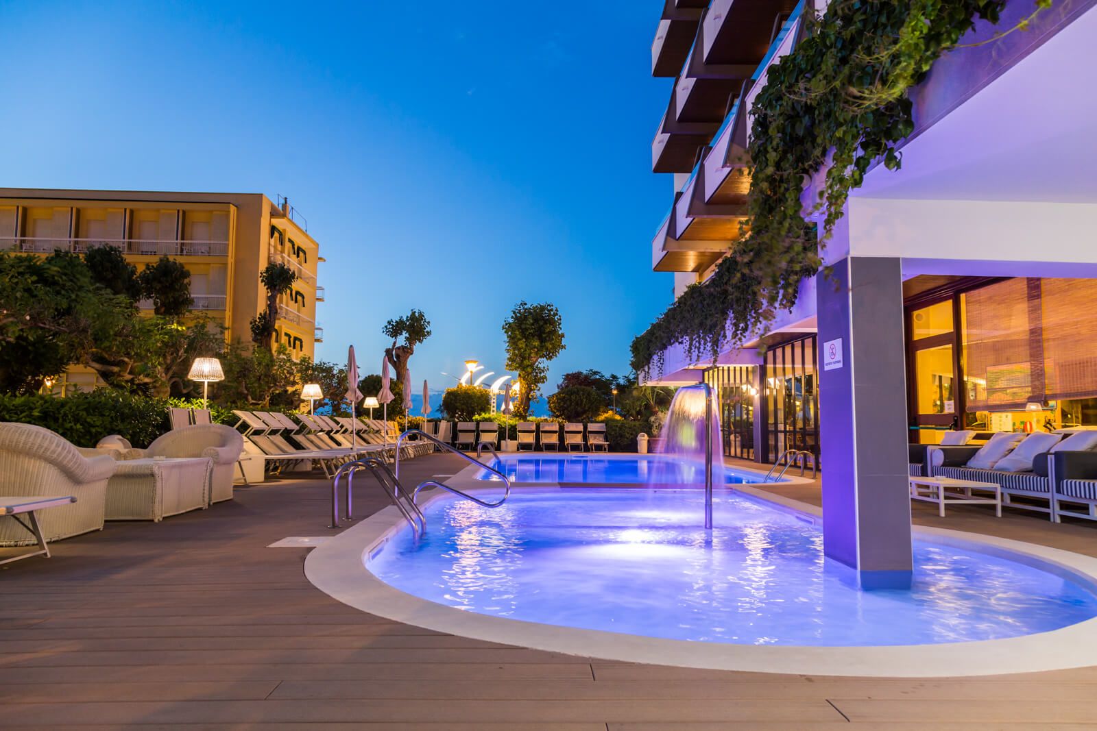 Moderne Poollandschaft im Freien, umgeben von bequemen Liegen und einem eindrucksvollen Abendhimmel.