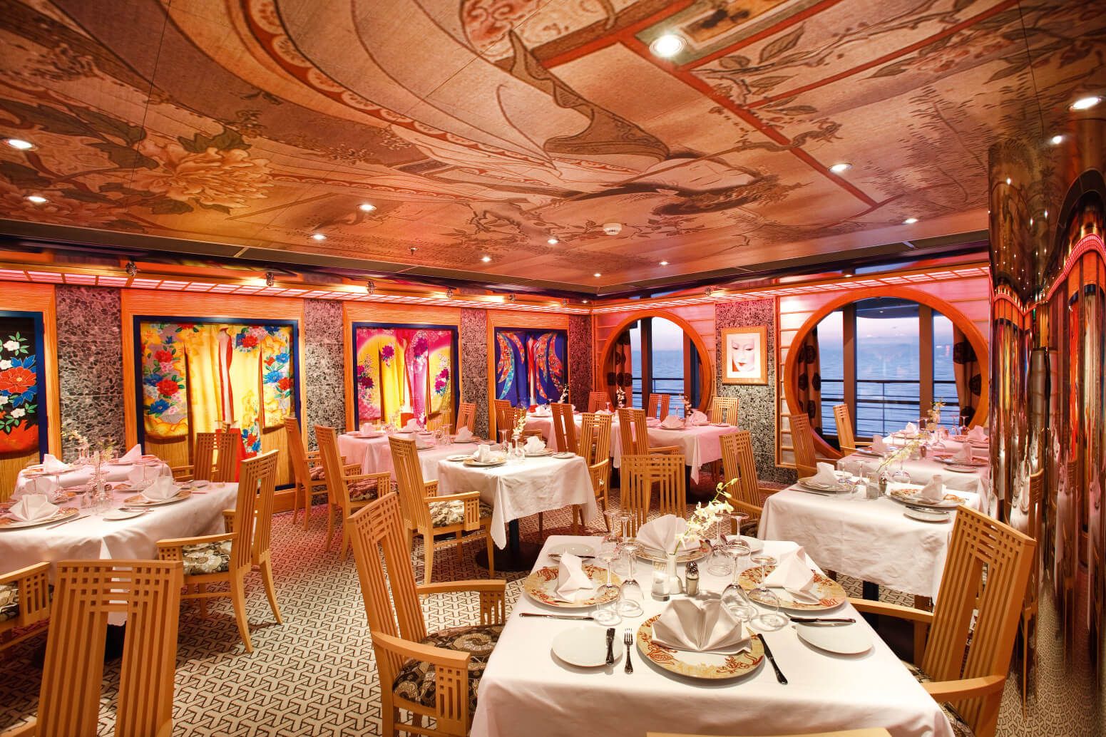 Elegantes Restaurant mit stilvollen Tischen, bunten Kunstwerken und Blick aufs Meer. Ruhige Atmosphäre.