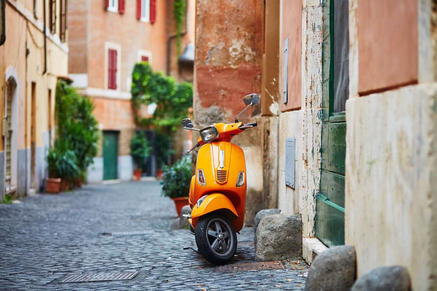 Eine leuchtend orangefarbene Vespa steht an einer alten, gepflasterten Gasse mit schönen Pflanzen.