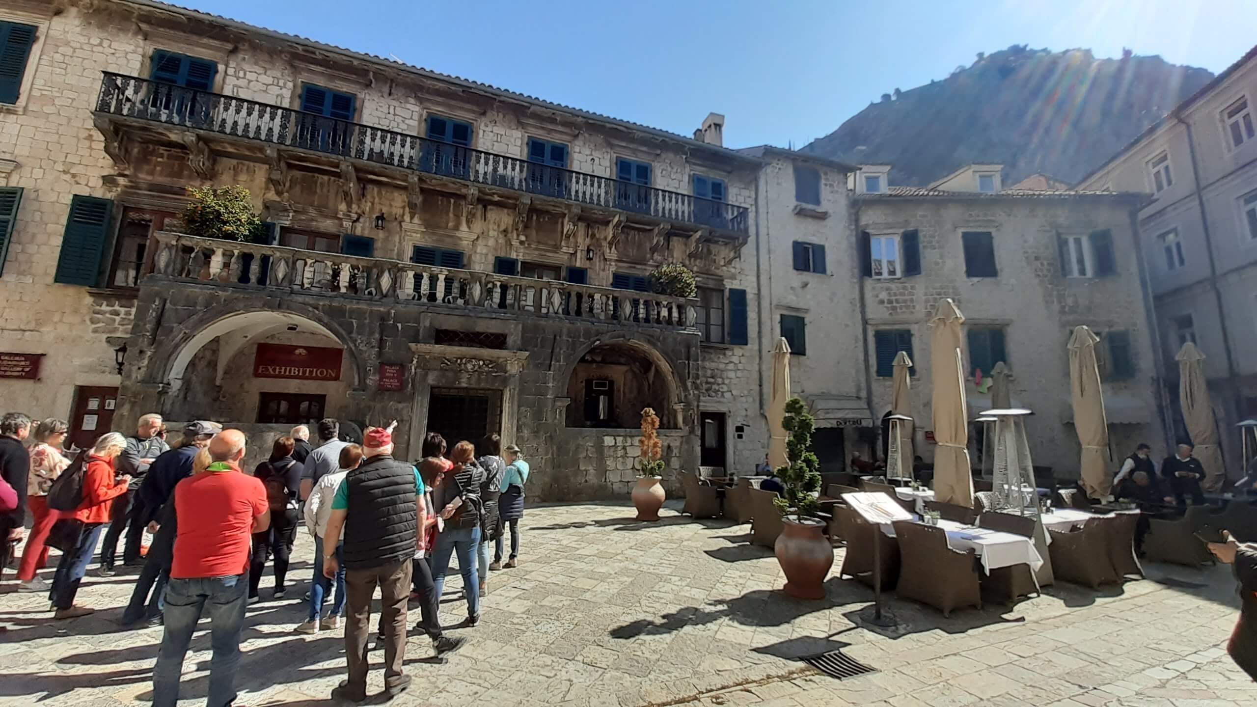 Ein belebter Platz mit historischen Gebäuden, Cafés und Besuchern in der Sonne. Einladende Atmosphäre.