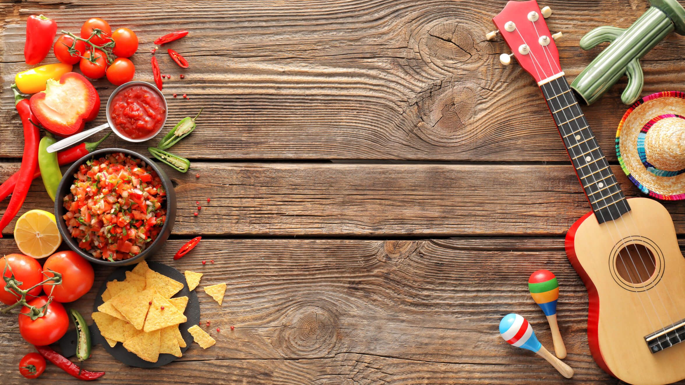 Bunte Zutaten für Salsa, Tortilla-Chips und musikalische Elemente auf einem rustikalen Holztisch.